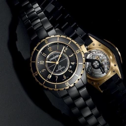 Close-up product photograph of a black ceramic luxury wristwatch with gold bezel and dial accents against a dark background