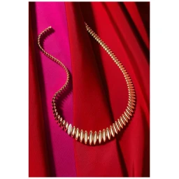 Gold statement necklace resting on vibrant draped red and pink silk fabric backgrounds