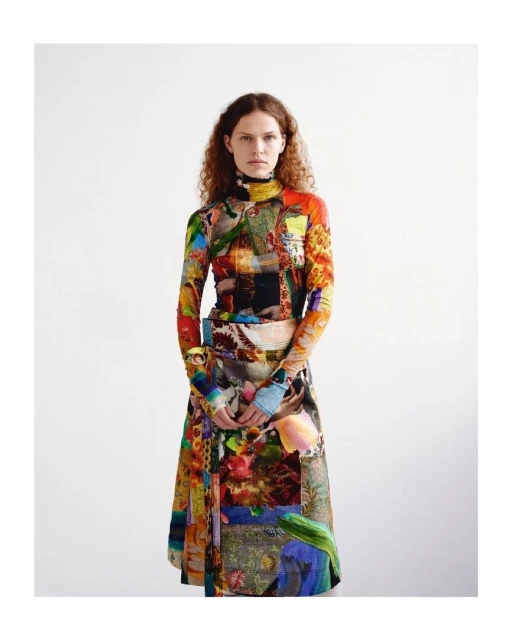 Adult female fashion model stands in a brightly colored long-sleeved top and a-line skirt with a white background in a studio setting.