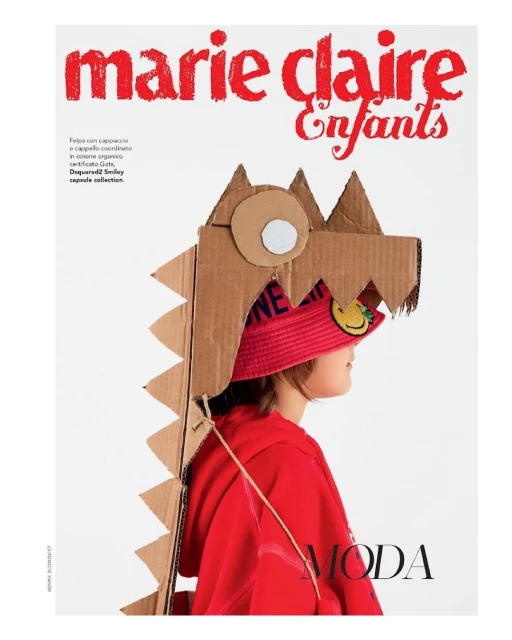 Child in red hoodie wearing a cardboard dinosaur headpiece and a smiley-face hat for Marie Claire Enfants fashion editorial.