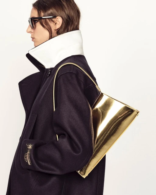 Fashion shot featuring a woman in a dark coat with a large white collar carrying a gold handbag, accessorized with sunglasses.