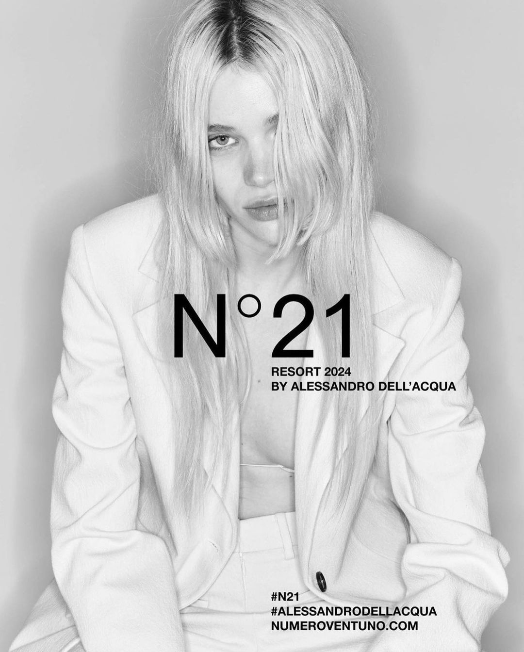 Monochrome fashion portrait of a blonde woman wearing a light-coloured blazer against a plain white background.
