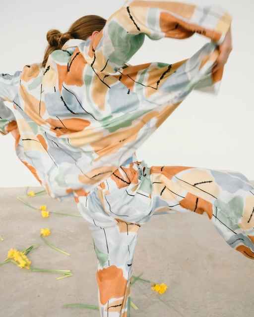 Woman in colorful patterned pajamas poses in a light studio with scattered yellow daffodils in a fashion or editorial style image.