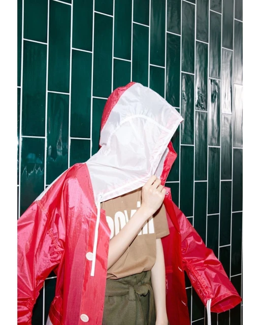 Person in a red hooded jacket against a green tiled wall, fashion and style in an indoor setting with bright lighting.