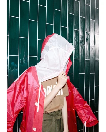 Person in a red hooded jacket against a green tiled wall, fashion and style in an indoor setting with bright lighting.
