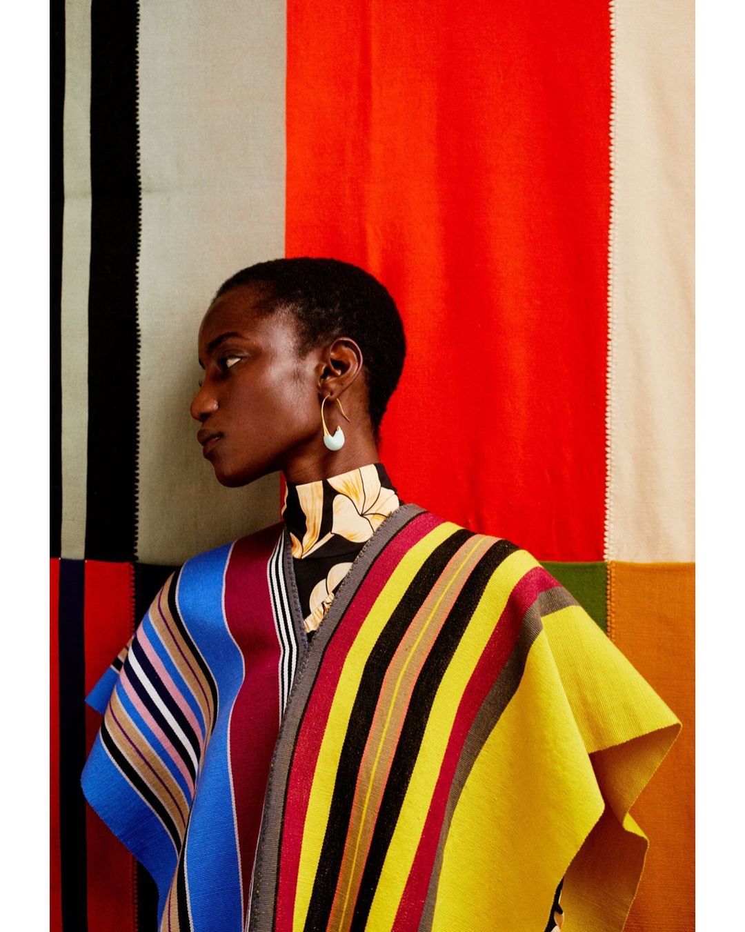 Elegant Black woman in a colorful striped poncho against a backdrop of red, black, cream, and green color blocks. Fashion editorial.