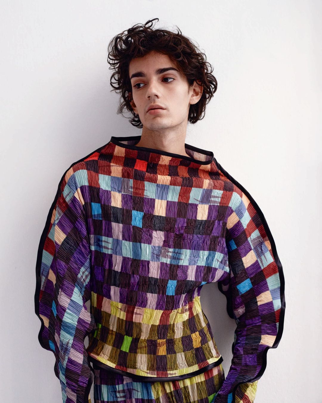 Young adult male wearing a multicolor patterned shirt in a fashion portrait against a neutral backdrop, showcasing fabric texture and color.