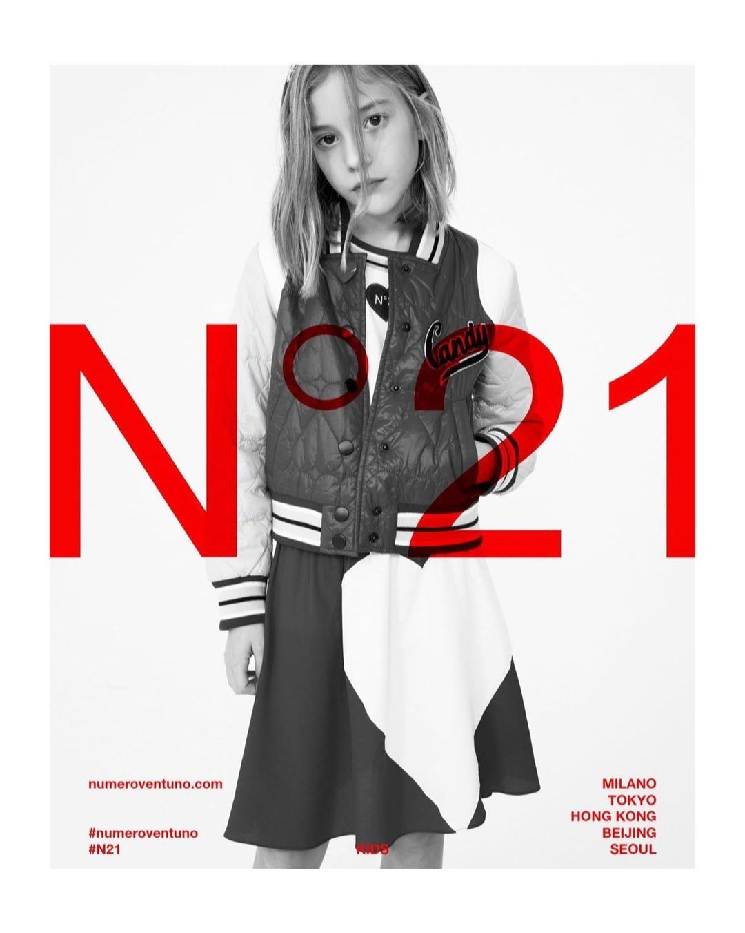 A young female child model wearing a varsity jacket and dark skirt against a white studio background with large red typography overlay.