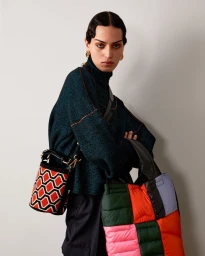 Model in dark turtleneck wearing patterned bucket bag and quilted tote bag against a neutral background