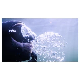 Close-up underwater portrait of a diver exhaling air bubbles in murky water