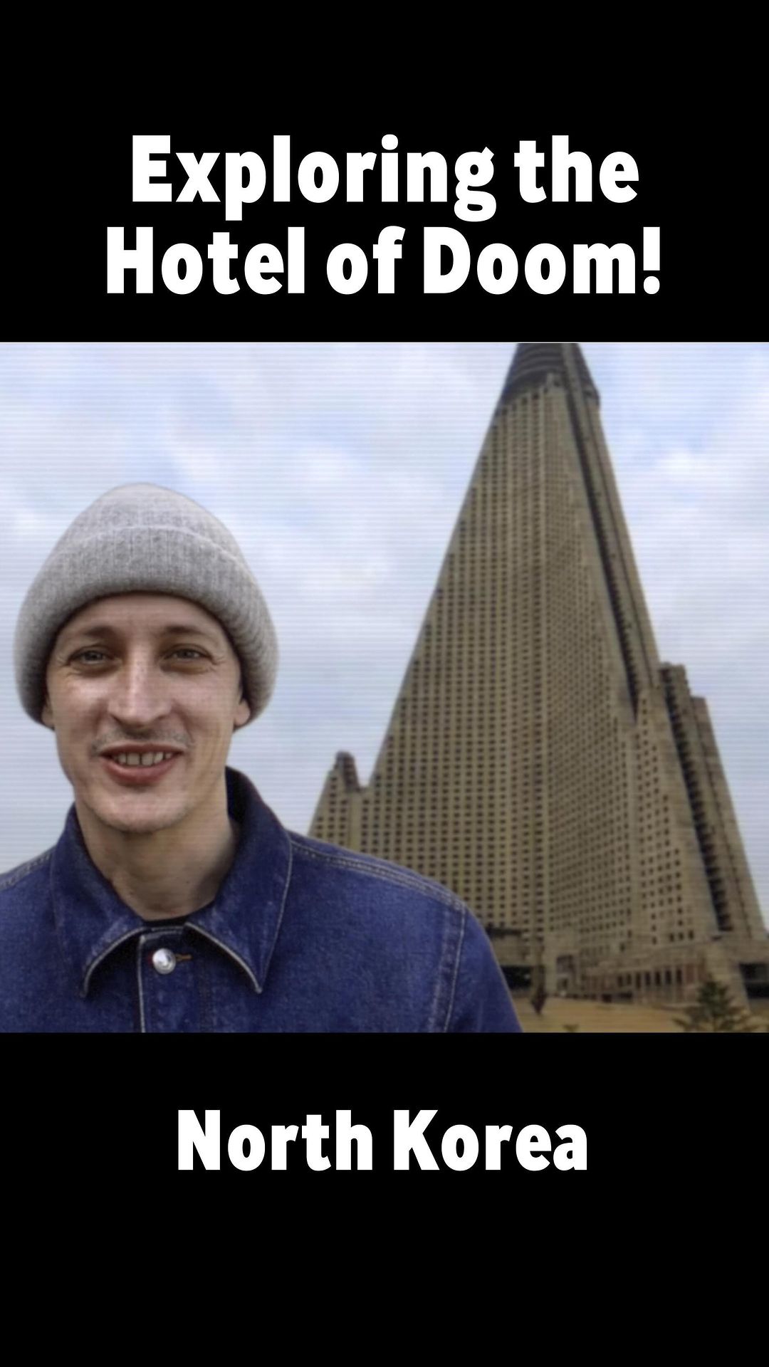 Man in beanie and denim jacket stands in front of Ryugyong Hotel, North Korea. Tall, pyramid-shaped building. Cloudy sky backdrop.