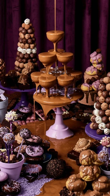 Extravagant chocolate dessert table featuring towers of chocolate truffles, glazed donuts, and champagne glasses filled with chocolate sauce.