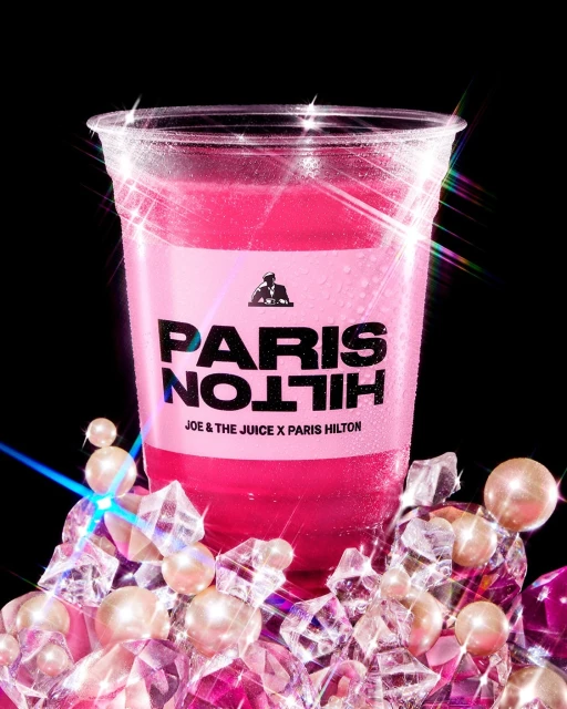 Studio shot of a pink-colored beverage in a plastic cup with ice and pearls, prominently featuring the logo of Paris Hilton.