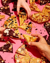 Multiple hands picking up triangular slices of loaded baked goods on a vibrant pink background