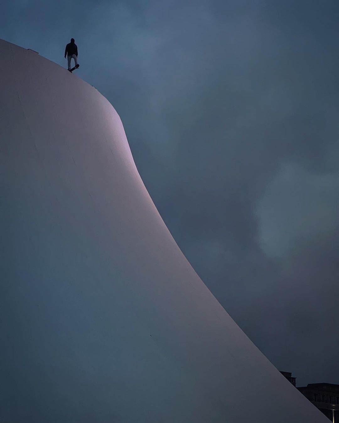 Lone figure walks on the white marble wall of the Oscar Niemeyer Museum against a dark sky, creating a stark contrast and minimalist scene.