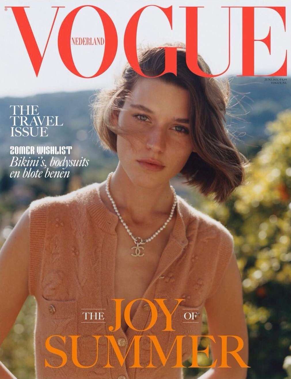 Vogue Nederland magazine cover featuring a young woman in a cardigan and pearl necklace against a green outdoor background.