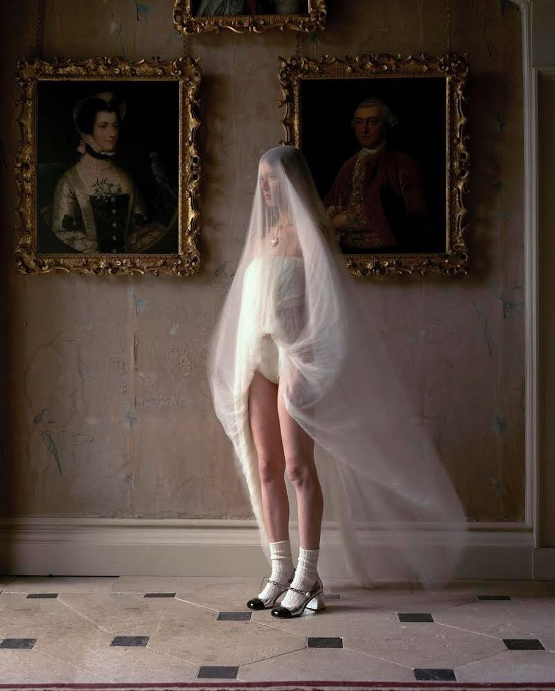 Fashion photography of woman in tulle with vintage portraits. Woman is wearing Mary Jane heels, and white socks in an indoor environment.
