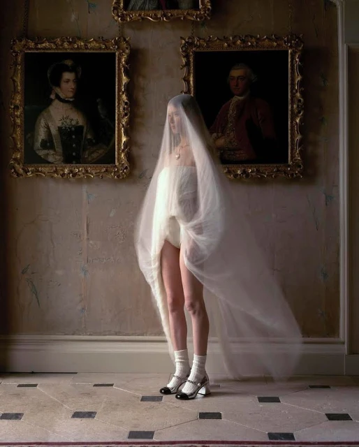 Fashion photography of woman in tulle with vintage portraits. Woman is wearing Mary Jane heels, and white socks in an indoor environment.