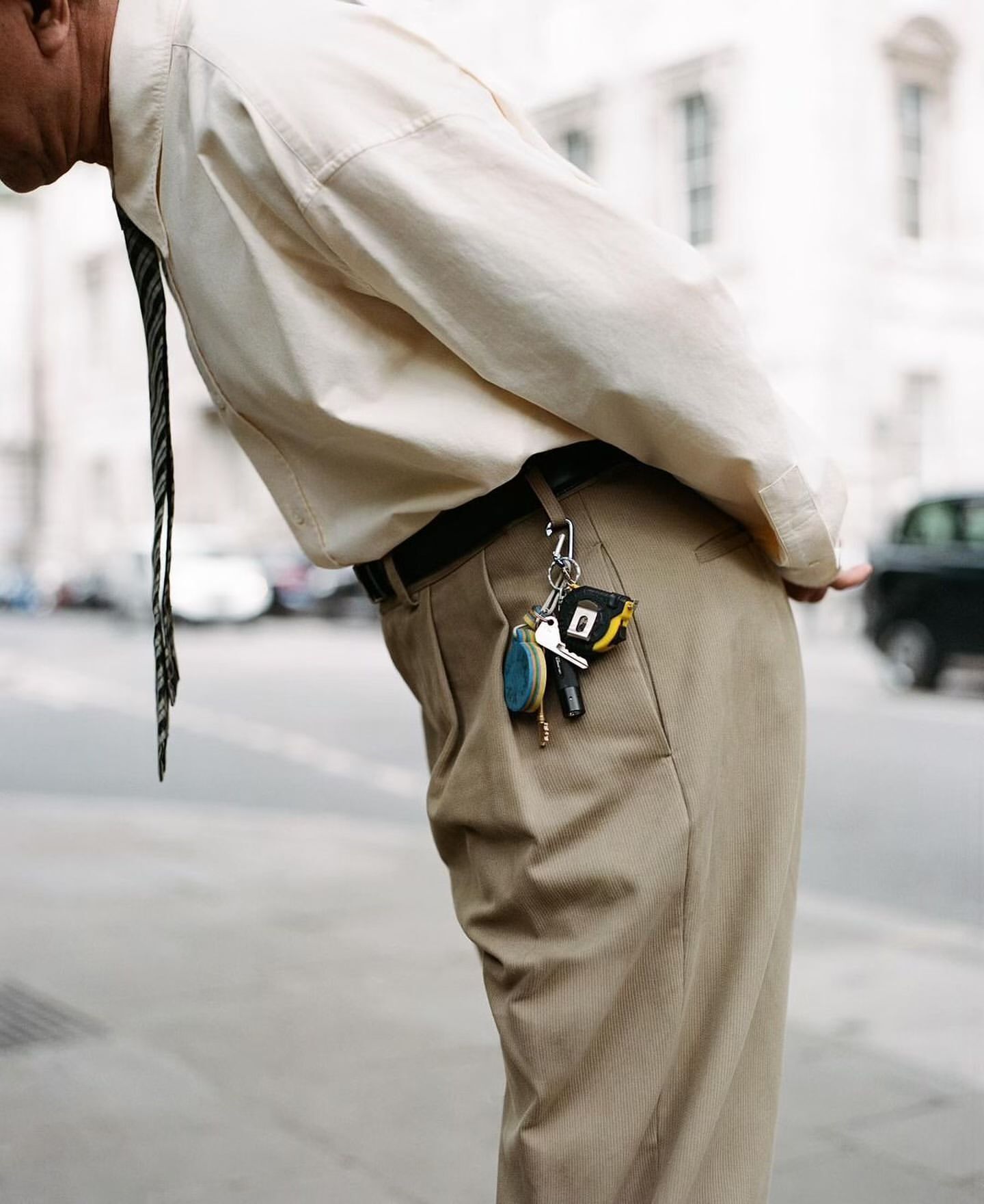 Waist-down shot of a man bending over, wearing a beige shirt, khaki pants, and tie, with keys hanging from his belt loop.