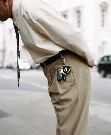 Waist-down shot of a man bending over, wearing a beige shirt, khaki pants, and tie, with keys hanging from his belt loop.