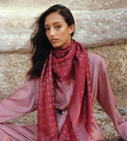 A woman wearing a patterned red scarf and striped outfit outdoors against a rocky background