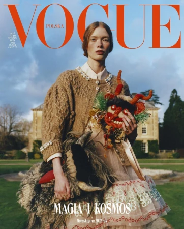 Vogue Polska cover featuring a red-haired model in a tan cardigan, holding a Krampus mask and a sheepskin creature against an outdoor backdrop.