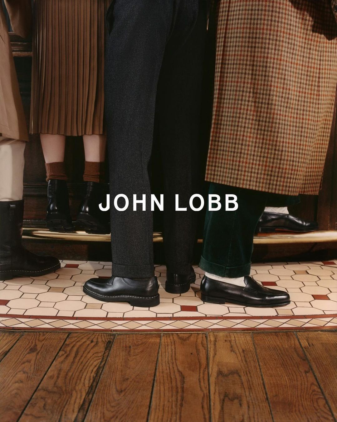 Several people standing on a tiled floor wearing formal shoes and dark-colored pants. Text overlay of the brand name "John Lobb."