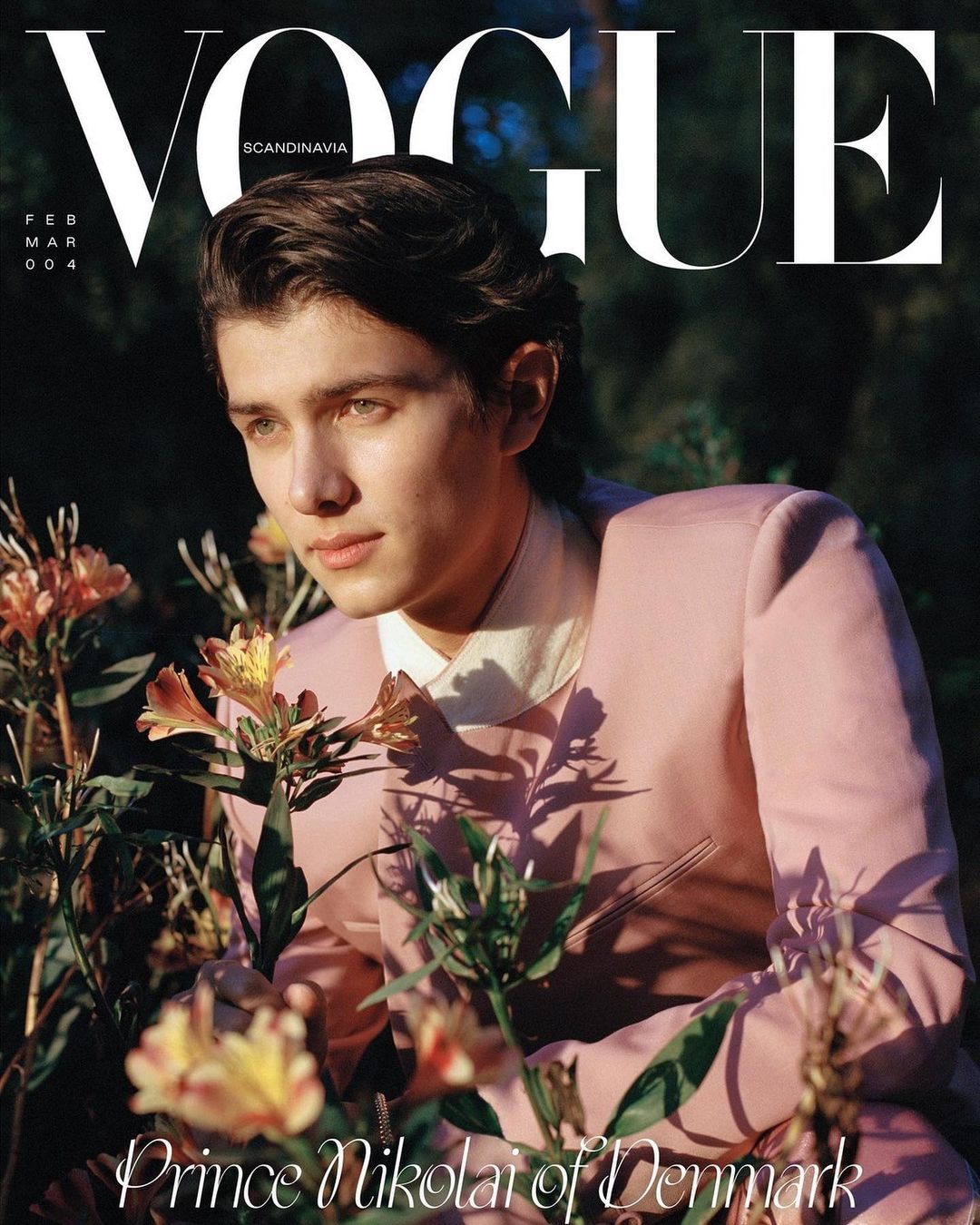 Vogue Scandinavia cover featuring Prince Nikolai of Denmark in a pink suit surrounded by flowers and greenery in an outdoor setting.