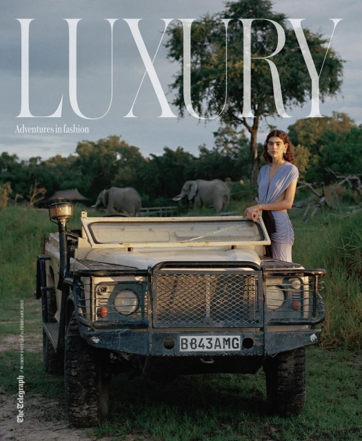 Magazine cover featuring a model leaning on a safari vehicle in a grassy landscape with elephants in the background under a cloudy sky.