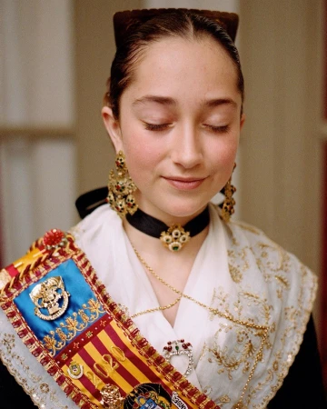 Close-up of a young woman with her eyes closed, wearing traditional attire with ornate jewelry and a colorful sash.