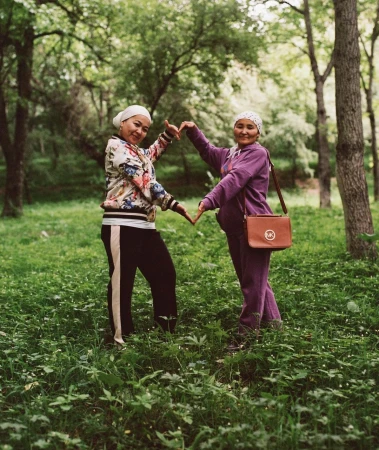 Two women standing in a lush green park making a heart shape with their hands, photographed by Hill & Aubrey.