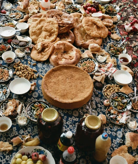 Overhead shot of a table laden with traditional Uzbek food, including flatbreads, fruits, nuts, salads, and beverages on a patterned cloth.