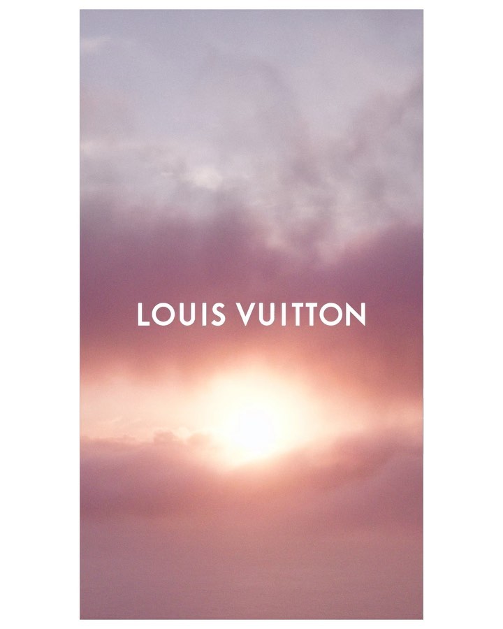 Sunrise or sunset with clouds in shades of pink and orange, featuring the Louis Vuitton brand name in white sans-serif typeface.