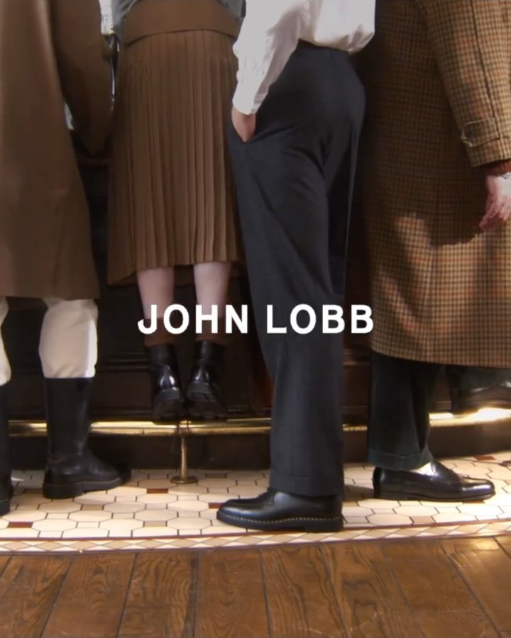 Low angle shot of people standing in a row wearing dress shoes and boots near a wooden bar with John Lobb text overlay.