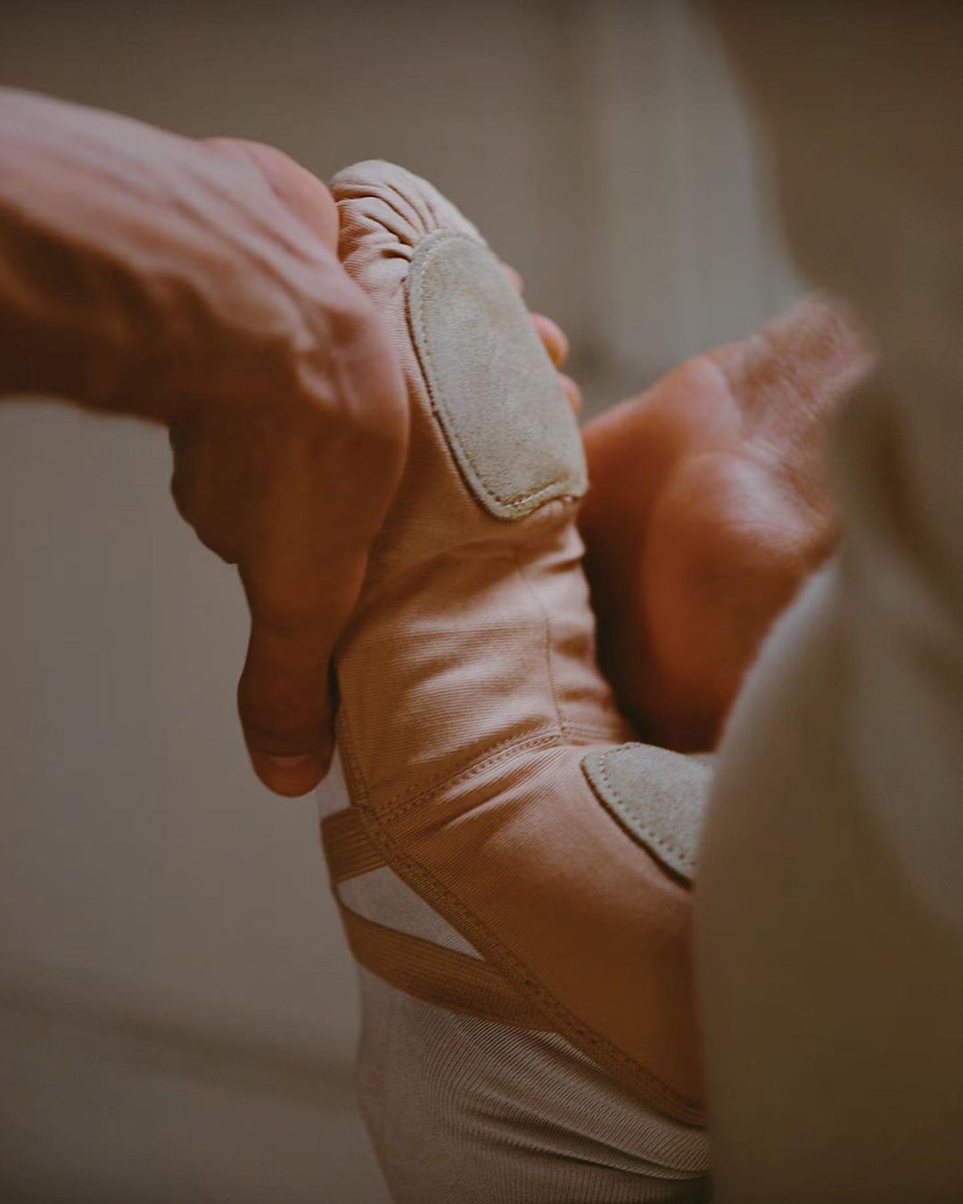 Close-up studio shot showcasing a pair of hands adjusting a pink ballet shoe, highlighting the texture and form of the footwear.