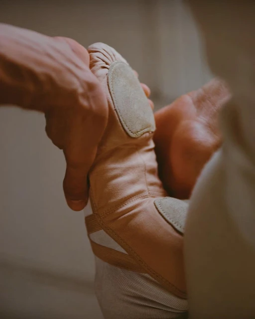 Close-up studio shot showcasing a pair of hands adjusting a pink ballet shoe, highlighting the texture and form of the footwear.
