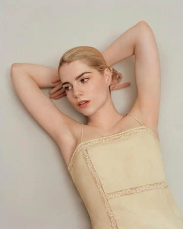 Blonde woman wearing a cream spaghetti strap top with lace trim posing with her arms raised against a plain background
