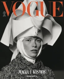 Black and white portrait of a model wearing an elaborate sculptural white headpiece and textured knit sweater.