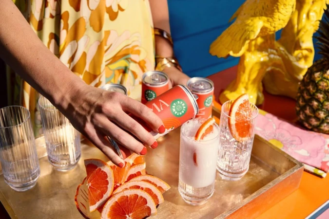 A person pours a Viva sparkling beverage into a glass with grapefruit slices, featuring vibrant yellows and oranges in a cheerful setting.
