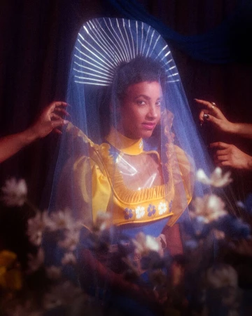 Portrait of a woman wearing a yellow dress and a translucent blue veil with a halo-like headpiece, photographed by Holly Andres.