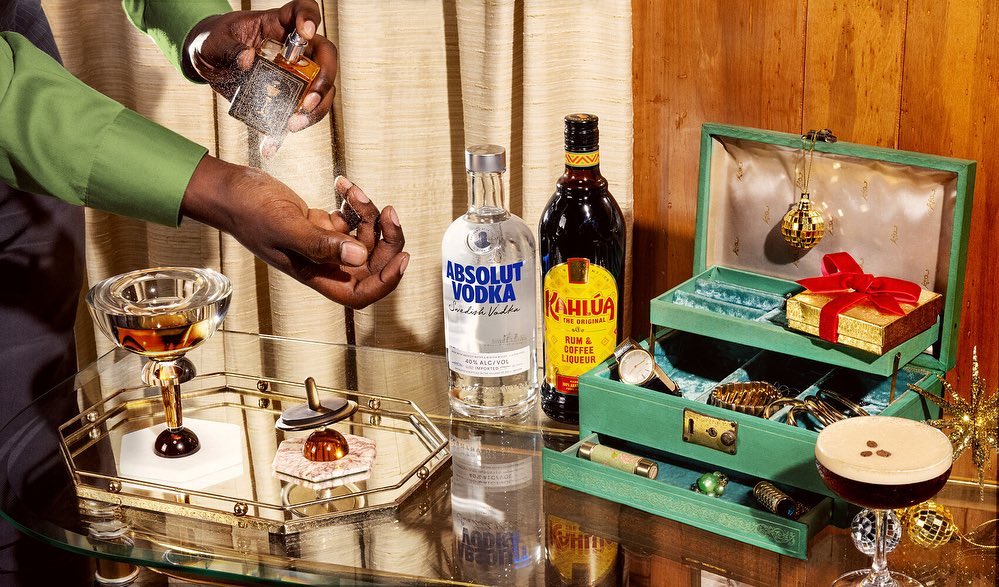 Cocktail drink preparation on a mirrored service tray with various liquors alongside a gift box, watch, and other accessories.