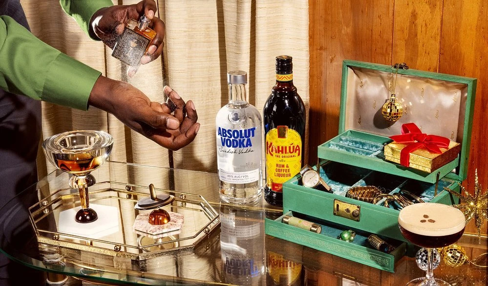 Cocktail drink preparation on a mirrored service tray with various liquors alongside a gift box, watch, and other accessories.