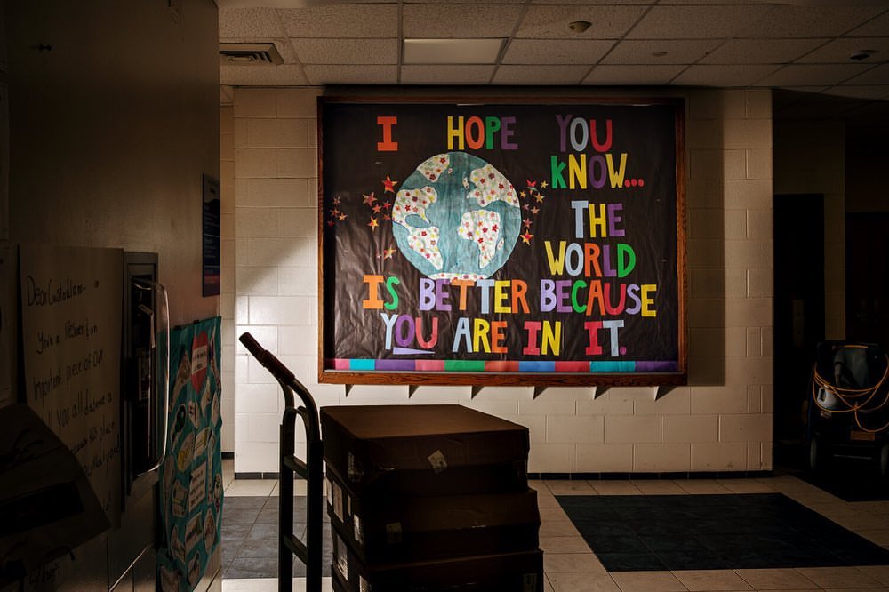 Bulletin board in a school hallway features colorful typography and an illustration of the world with positive message about being in it.