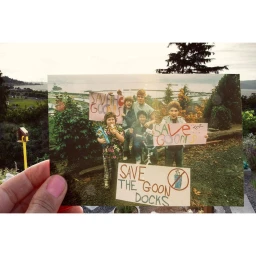 Hand holding a photograph of a group of young people holding handmade Save the Goon Docks signs outdoors.