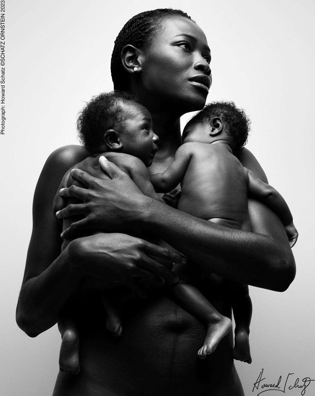 Striking black and white portrait of an African woman tenderly holding two newborn babies, showcasing maternal love and connection.