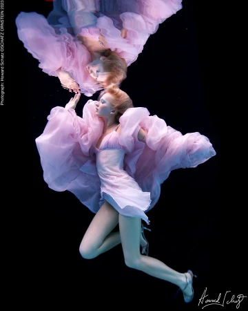 Underwater portrait by Howard Schatz of a woman in a flowing pink dress floating beneath the water surface with reflection