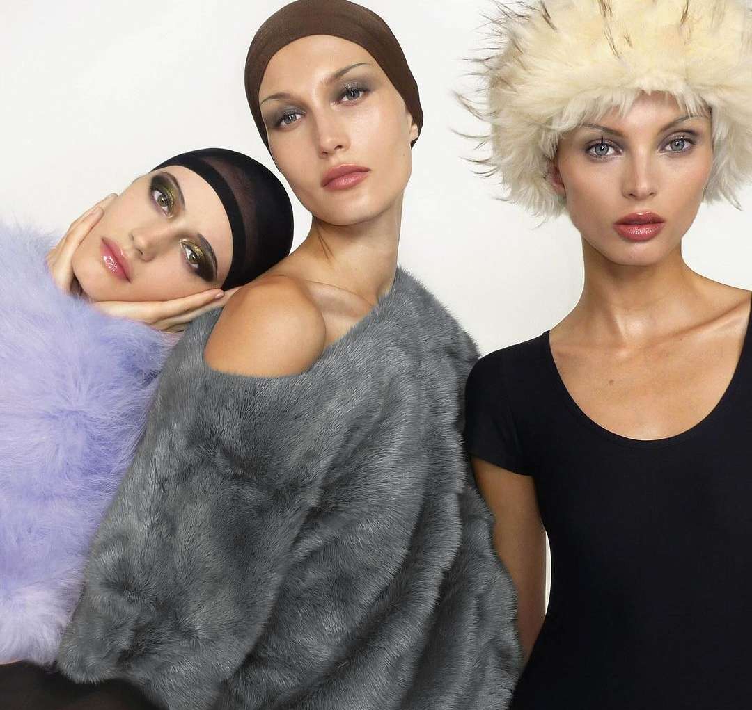 Three female fashion models posing in a photo studio. Two models wear fur coats and head coverings. One model wears a black top and fur hat.