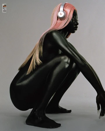 Woman with dark skin tone squats in a studio with pink hair and silver Beats headphones. The image has a plain gray background.