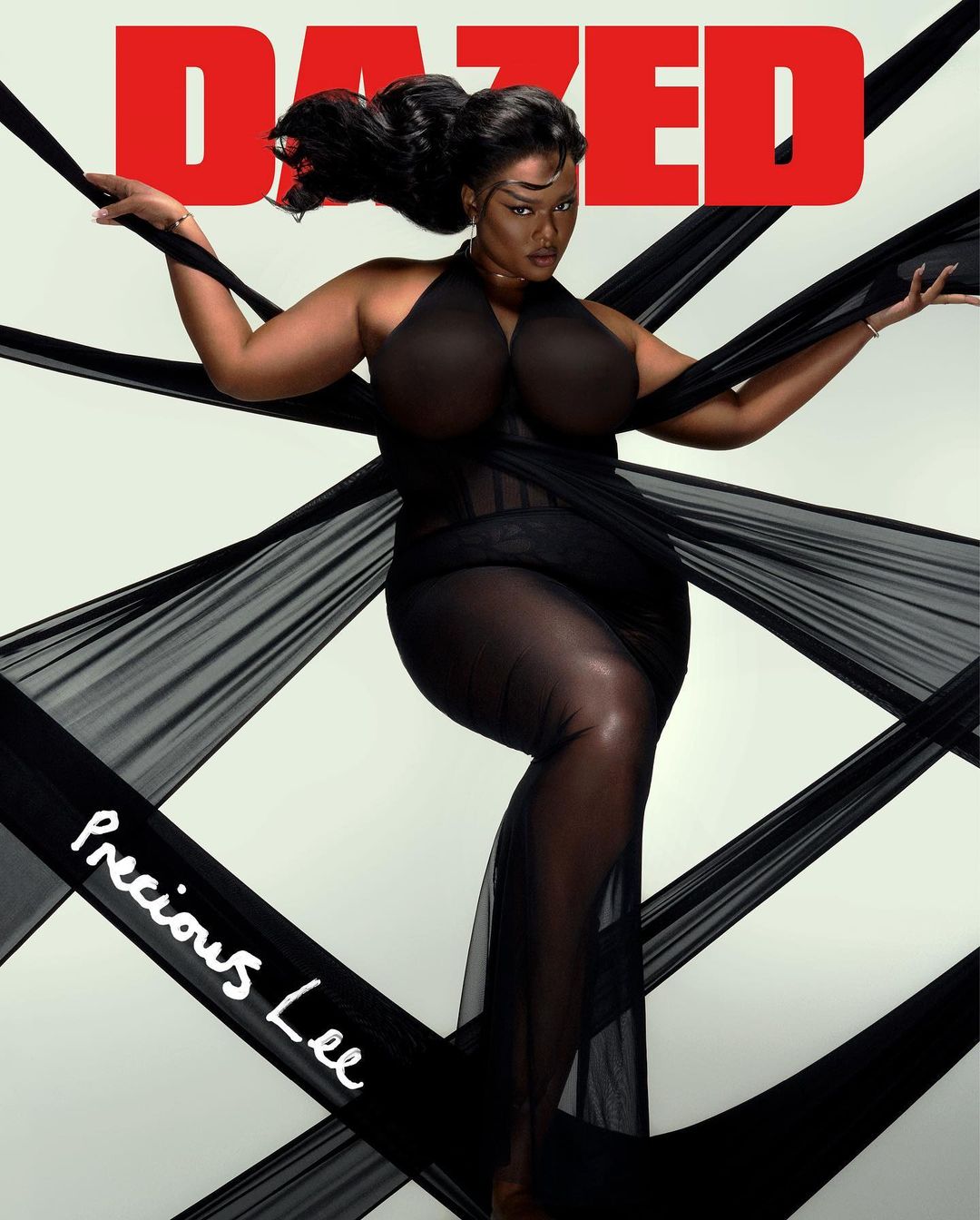 An adult woman is featured on a magazine cover wearing a black dress with black sheer fabric in a studio setting, shot at eye-level.