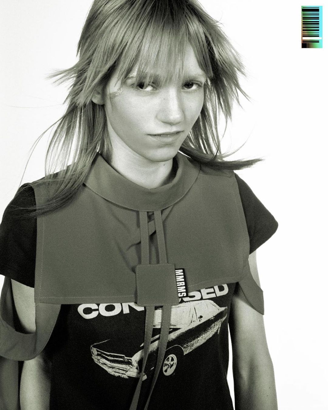 Monochrome portrait of a young woman with bangs wearing a bib-style collar over a t-shirt with a car graphic against a white backdrop.